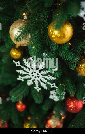 Detailansicht der schönen grünen Zweige der Weihnachtsbaum mit hellen goldenen und roten Kugeln dekoriert, weiß Große und Kleine Schneeflocken. Vertikale Farbe Stockfoto