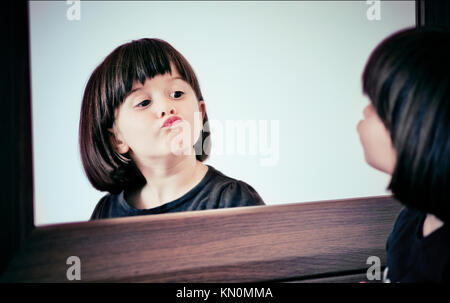 Hübsches kleines Mädchen 2-4 Jahre machen lustige Gesichter in den Spiegel, auf ihr Spiegelbild. Stockfoto