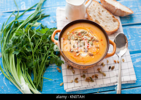 Selbstgemachte Kürbissuppe mit Sahne, Brot, grünen und Kürbiskerne auf einer hölzernen Hintergrund. Ansicht von oben. Stockfoto