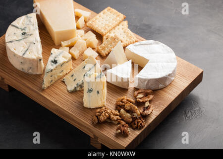 Verkostung Käse Teller auf eine Holzplatte mit Walnüssen und Cracker. Essen für Wein und romantisch, Käse Feinkost auf einem dunklen Stein Tabelle. Stockfoto