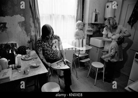 1970er Slum-Gehäuse, Küche dient auch als Badezimmer. Die Familie isst zusammen. Armut. Ascot Gas-Wasser-Boiler an der Wand über dem Butler Spüle 1972 Fulham, England 70s UK HOMER SYKES Stockfoto