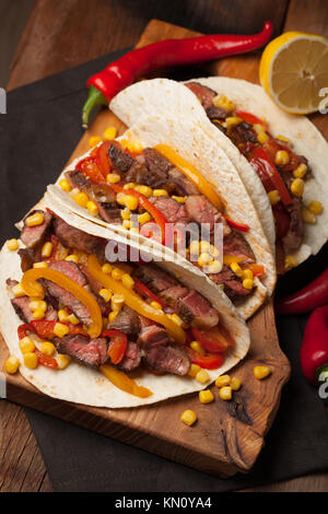 Drei Mexikanische Tacos mit Marmor, Black Angus Rindfleisch und Gemüse auf alten rustikalen Tisch. Mexikanische Gerichte mit Soßen Guacamole und Salsa in Schalen. Stockfoto