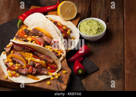 Drei Mexikanische Tacos mit Marmor, Black Angus Rindfleisch und Gemüse auf alten rustikalen Tisch. Mexikanische Gerichte mit Soßen Guacamole und Salsa in Schalen. Stockfoto