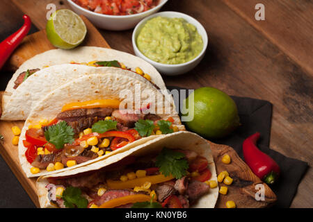 Drei Mexikanische Tacos mit Marmor, Black Angus Rindfleisch und Gemüse auf alten rustikalen Tisch. Mexikanische Gerichte mit Soßen Guacamole und Salsa in Schalen. Stockfoto