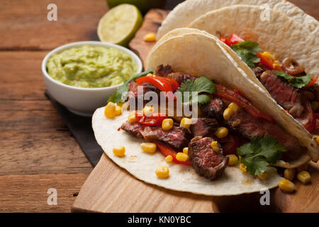 Drei Mexikanische Tacos mit Marmor, Black Angus Rindfleisch und Gemüse auf alten rustikalen Tisch. Mexikanische Gerichte mit Soßen Guacamole und Salsa in Schalen. Stockfoto