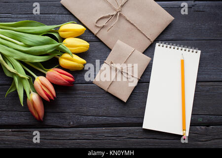 Leer notebook, Bleistift und gelbe und rote Tulpen Blumen auf vintage Holz- Hintergrund. Selektive konzentrieren. Für Text platzieren. Flach. Stockfoto