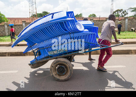 Einen kenianischen Mann ziehen einen Handkarren entlang einer Straße, die Plastikstühle, Nairobi, Kenia, Ostafrika Stockfoto