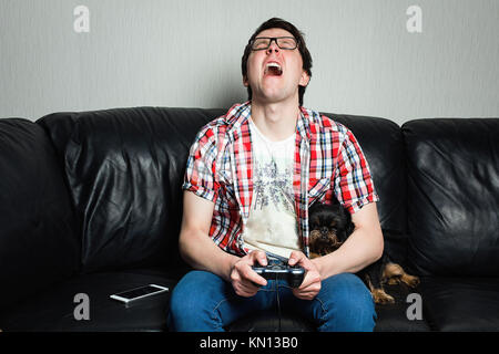 Ein junger Mann in einem roten T-Shirt und Blue Jeans sitzt zu Hause und spielt Videospiele zusammen mit ihren Hunden. Armer Kerl ist weinend und wütend, weil der scheitern. t Stockfoto