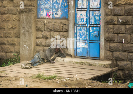 Eine kenianische Obdachloser in Zerzausten schmutzige Kleidung liegt an der Seite eines Gebäudes, Nairobi, Kenia, Ostafrika Stockfoto