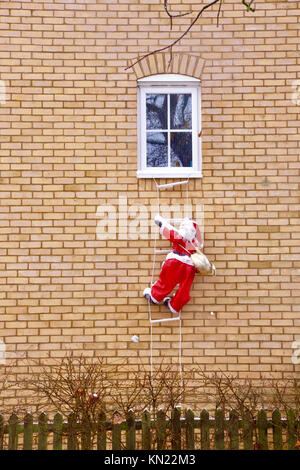 Weihnachtsmann entdeckt in Suffolk eine Leiter nach oben klettern auf dem Weg zu einem Haus Fenster. Frohe Weihnachten an alle! Stockfoto