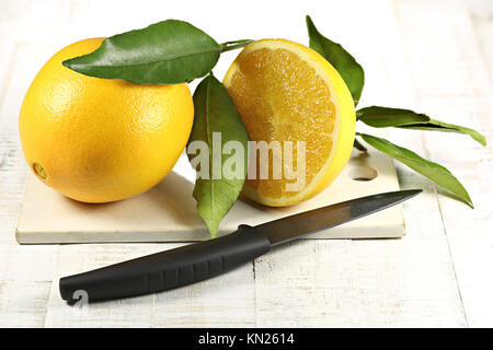 Orangen mit Blättern auf altem Schneidebrett Stockfoto