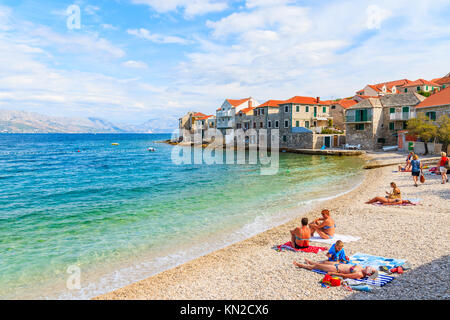 Stadt Postira, Insel Brac - Sep 7, 2017: Touristen Sonnenbaden am Strand in Postira Stadt mit alten Häusern am Ufer, Insel Brac, Kroatien. Stockfoto