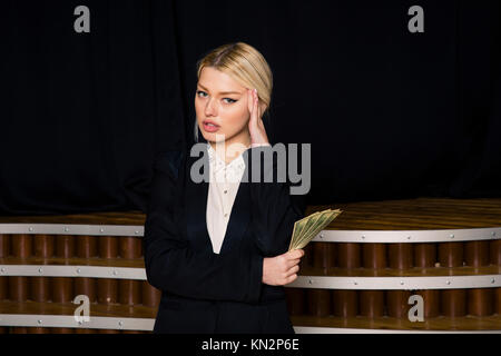 Schöne blonde Geschäftsfrau mit Geld an loft Büro im schwarzen Anzug. Stockfoto