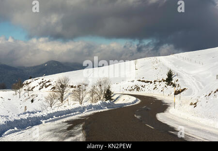 A snowy road curve in the Vosges mountains (France) in winter with a cloudy sky. Stockfoto