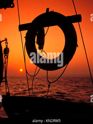 Sonnenuntergang auf dem Meer Blick durch die Silhouette der Takelage und Rettungsring eines traditionellen Themse Segelschiff, English Channel, Großbritannien Stockfoto