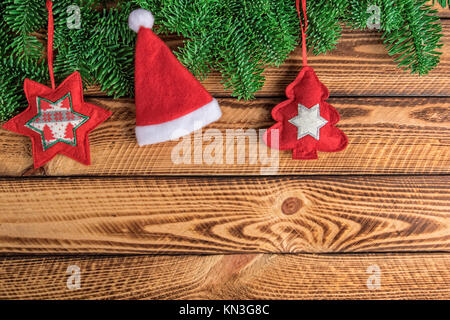 Weihnachten Hintergrund mit Weihnachtsmütze tanne Zweig und rotem Filz Dekoration über dunkle Holzbohlen Stockfoto