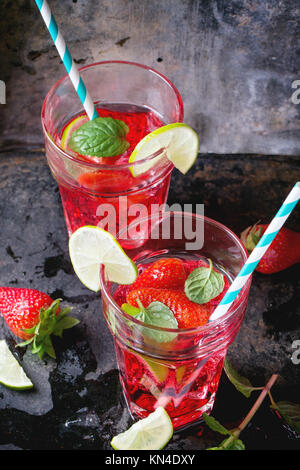 Zwei Gläser mit Retro cocktail Rohre mit hausgemachten Erdbeer Limonade, serviert mit frischen Erdbeeren, Minze, Limette und Eiswürfel overdark Hintergrund. Stockfoto