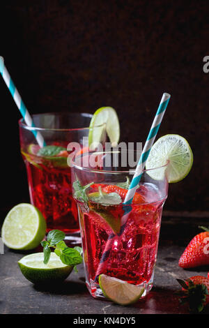 Zwei Gläser mit Retro cocktail Rohre mit hausgemachten Erdbeer Limonade, serviert mit frischen Erdbeeren, Minze, Limette und Eiswürfel overdark Hintergrund. Stockfoto