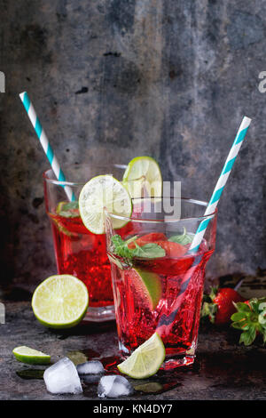 Zwei Gläser mit Retro cocktail Rohre mit hausgemachten Erdbeer Limonade, serviert mit frischen Erdbeeren, Minze, Limette und Eiswürfel overdark Hintergrund. Stockfoto