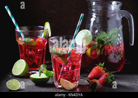 Zwei Gläser mit retro Cocktail Rohre und glaskanne von Erdbeer Limonade, serviert mit frischen Erdbeeren, Minze und Limette über dunklen Hintergrund. Siehe se Stockfoto