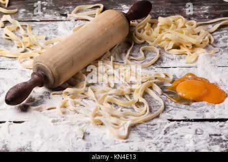 Hausgemachte Teigwaren mit Mehl, rohes Eigelb und Vintage Nudelholz über alten Holztisch. Serien ansehen Stockfoto