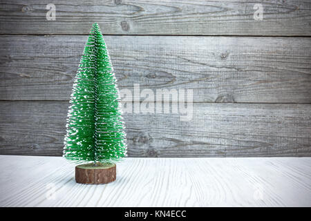 Kleine künstliche Weihnachtsbaum auf weißem Holz gegen rustikalen grau Boards Stockfoto