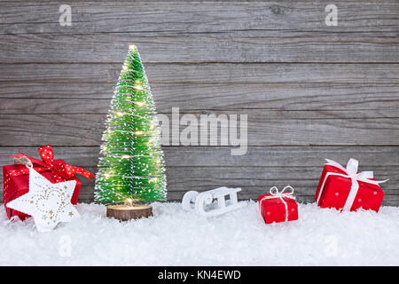 Festlich beleuchtete Weihnachtsbaum mit roten Geschenkboxen, Schlitten und Stern auf Schnee Stockfoto