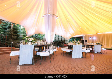 Restaurant, Engagement, Innenraumkonzept. Unter riesigen gelben Zelt es gibt Tische in vintage Stil dekoriert mit Blumen und Snowy White Geschirre Stockfoto