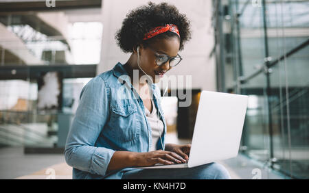 Lächelnden jungen afrikanischen weibliche Studenten sitzen auf einem Campus Bank arbeitet an einem Laptop während der Vorbereitung für die Prüfung Stockfoto