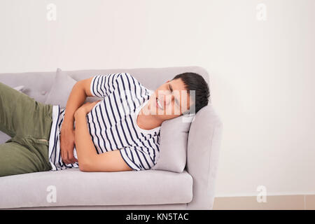 Hübscher junger Mann leidet unter Bauchschmerzen, während auf dem Sofa zu Hause liegen Stockfoto