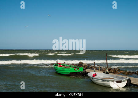 Zwei leere Angeln rudern Boote tided zu einem kleinen Pier mit Wellen auf und blauer Himmel über. Stockfoto