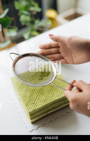 Gießen grüner Tee Pulver über leckeren Käsekuchen Stockfoto