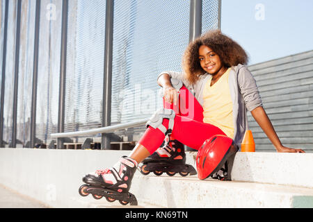 Happy afrikanisches Mädchen sitzen auf der Treppe in rollschuhen an rollerdrom Stockfoto