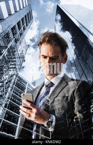 Doppelt belichtete Bild von einem Geschäftsmann mit Mobiltelefon und Wolkenkratzer mit Baustellen Stockfoto