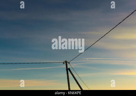 Telefonmast und Kabel wie ein Flugzeug fliegt von einem gegenwärtigen Mond bei Sonnenuntergang Stockfoto