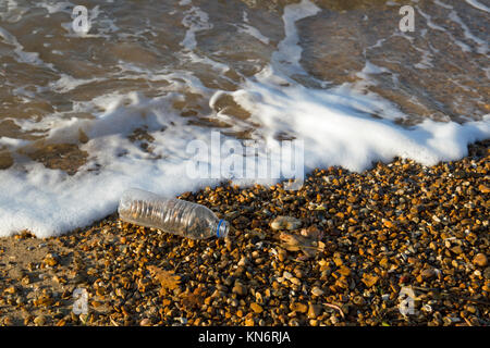 Einen durchsichtigen leer 500 ml Flasche auf einen Kiesstrand mit Wellen um Sie herum. Stockfoto