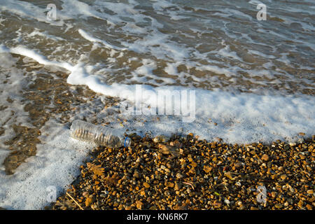 Einen durchsichtigen leer 500 ml Flasche auf einen Kiesstrand mit Wellen um Sie herum. Stockfoto