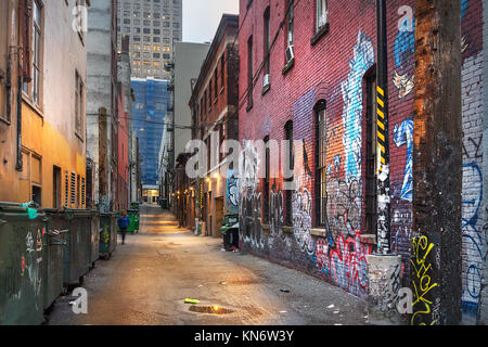 Eine schmale Gasse zwischen farbigen alten Backsteinbauten und Müllcontainer am Abend an der Vancouver Downtown. Stockfoto