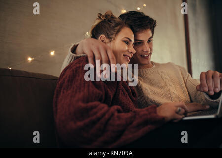 Entspannt Mann und Frau mit Laptop sitzen auf einem Sofa. Paar mit Laptop im gemütlichen Wohnzimmer. Stockfoto