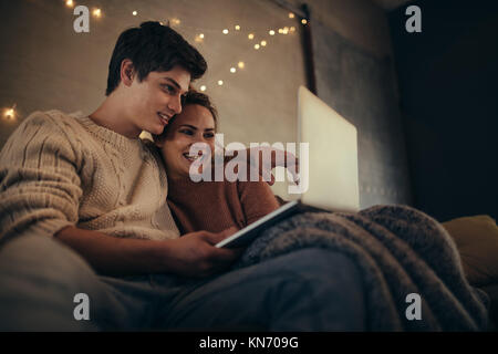 Lächelndes Paar mit Laptop im hygge Haus. Der Mann und die Frau sitzt auf einem Sofa mit einem Laptop im gemütlichen Wohnzimmer. Stockfoto