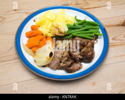 Englisch Abendessen langsam gekocht shoulderof Lamm Karotten Kartoffeln feine grüne Bohnen braten Zwiebel Zwiebeln serviert auf einem blauen und weißen Platte Holztisch Stockfoto