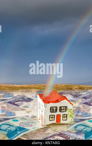 Hand gemalte Haus aus Stein sitzt auf britische Währung stellt mit einer echten Regenbogen endet an dem Haus vorschlagen Einsparungen bei der Stempelsteuer Stockfoto