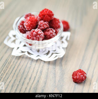 Gefrorene Himbeeren in eine Glasschüssel auf einem Holztisch. Stockfoto