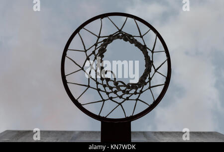 Auf der Suche nach oben durch einen Basketballkorb mit Netz an einem bewölkten Himmel Stockfoto