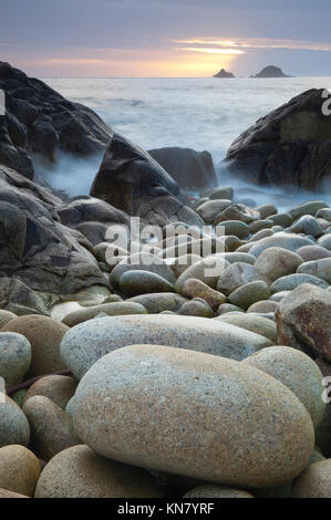 West Cornwall Meer bei Sonnenuntergang mit bewegtem Wasser rollen über große Strand bolder Steine Stockfoto