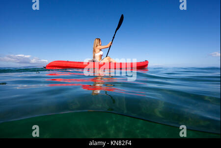 Gesunde weibliche Paddles ein rotes Kajak in Makena, Maui, Hawaii. 2 Ebenen anzeigen. Stockfoto