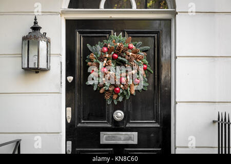 Eine festliche Weihnachten Kranz hängt an der Tür eines Hauses im Royal Borough von Kensington und Chelsea. London, Großbritannien. Stockfoto