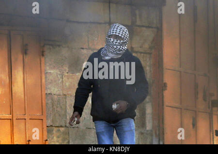 Dezember 11, 2017 - Hebron, West Bank, Palästina - einen palästinensischen Demonstrant schleudern stosnes gegenüber israelischen secrity Kräfte während der Auseinandersetzungen hinter einem Checkpoint im Zentrum der Stadt von der West Bank Stadt Hebron am 11. Dezember 2017, wie Demonstrationen weiterhin im Nahen Osten und anderswo über uns Präsident Donald Trump Erklärung von Jerusalem als Hauptstadt Israels zu Flare (Credit Bild: © Wisam Hashlamoun/APA Bilder über ZUMA Draht) Stockfoto