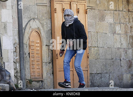 Dezember 11, 2017 - Hebron, West Bank, Palästina - einen palästinensischen Demonstrant schleudern stosnes gegenüber israelischen secrity Kräfte während der Auseinandersetzungen hinter einem Checkpoint im Zentrum der Stadt von der West Bank Stadt Hebron am 11. Dezember 2017, wie Demonstrationen weiterhin im Nahen Osten und anderswo über uns Präsident Donald Trump Erklärung von Jerusalem als Hauptstadt Israels zu Flare (Credit Bild: © Wisam Hashlamoun/APA Bilder über ZUMA Draht) Stockfoto