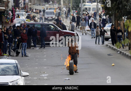 Dezember 11, 2017 - Hebron, West Bank, Palästina - eine maskierte Palästinensischen Demonstrant Rollen einen brennenden Reifen bei Auseinandersetzungen mit Israelischen secrity Kräfte hinter einem Checkpoint im Zentrum der Stadt von der West Bank Stadt Hebron am 11. Dezember 2017, wie Demonstrationen weiterhin im Nahen Osten und anderswo über uns Präsident Donald Trump Erklärung von Jerusalem als Hauptstadt Israels zu Flare (Credit Bild: © Wisam Hashlamoun/APA Bilder über ZUMA Draht) Stockfoto